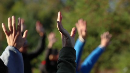 A group of people are exercising in a park. Seen is a close up of a group of hands slowly waving in the air with selective focus and beautiful light