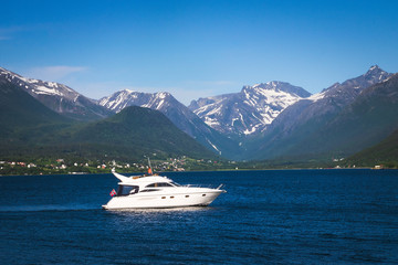 Beautiful mountains and fjord in Norway with a white pleasure boat on the calm blue water on a sunny day.