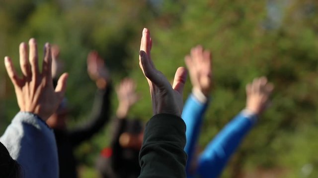 A group of people are exercising in a park. Seen is a close up of a group of hands slowly waving in the air with selective focus and beautiful light