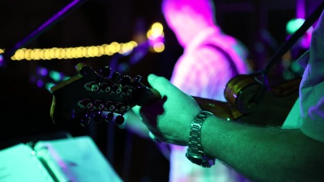 View of country music band with selective focus from behind the mandolin player. The view is to the back of the guitarist and to the dark auditorium