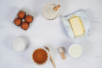 The ingredients for making a honey cake lie in a circle on a white table. Top view.