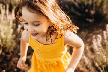 Close up of a lovely little girl running in a field of flowers laughing dressed in yellow dress .