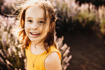 Portrait of a lovely little girl looking at camera laughing while being in a field of flowers...
