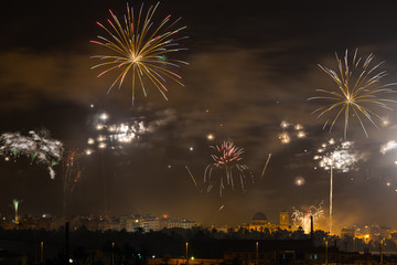 A big colorful firework in the summer in the spanish city Elche. A view over the night city with rockets and smoke in the air.