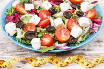 Tape measure and greek salad with feta cheese and vegetables as healthy meal containing vitamins