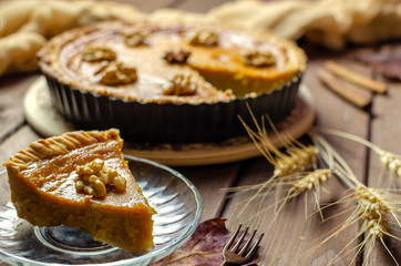 Pumpkin homemade vegan pie and spices cinnamon, anis, yelllow dry autumn leaves decor on dark table background.