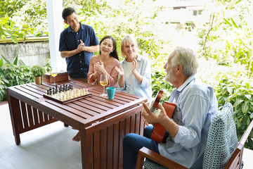 a group of multiethnic senior people playing guitar and sing a song after playing chess board with happy smiling face on sunny day