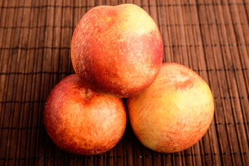Three fresh ripe organic nectarines on a wooden brown table, top view or flat lay photo of healthy fruits