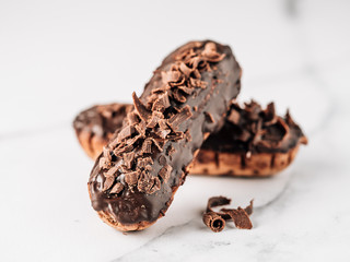 Homemade eclairs with chocolate on white marble background. Close up view of delicious healthy profitroles with chocolate glaze