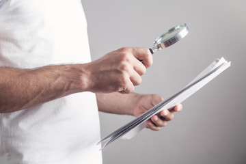 Man holding magnifying glass with documents.