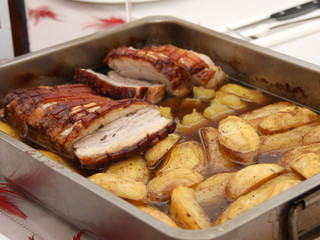 Homemade roast pork belly with fried potatoes sliced ​​in juice served in a roasting pan on a set table