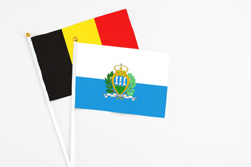 San Marino and Belgium stick flags on white background. High quality fabric, miniature national flag. Peaceful global concept.White floor for copy space.