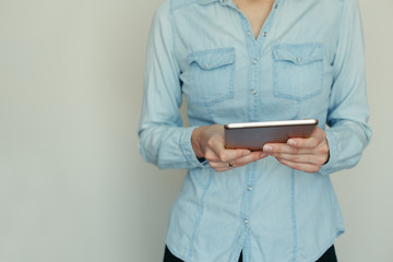 Image of a young woman working on a tablet computer at home on a background of light wall