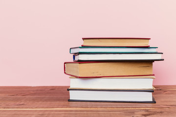 A simple composition of many hardback books, raw books on a wooden table and a pale pink background