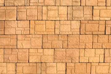 A yellow old scruffy wall made of beautiful artificial stone, shot in the evening at sunset. Abstract modern trendy texture background. Design element.
