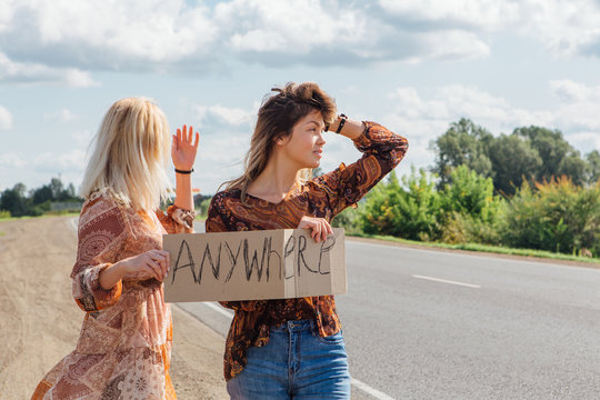 Two beautiful girls hitchhiking and vote with a sign ANYWHERE on road. Copy space.
