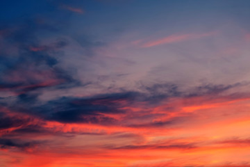 Light cirrus clouds at sunset are painted in bright fairy-tale fiery red, orange, golden, yellow colors against a dramatic dark blue sky. Abstract trendy modern texture background