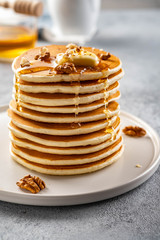 Tasty breakfast. Homemade pancakes with crushed walnut, honey or maple syrup on grey background.