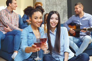 Group of friends having party indoors fun together two girls drinking wine cheers