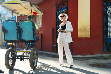 Stylish woman in a white suit and white hat on an city street of Cuba