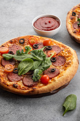 Tasty pepperoni pizza and cooking ingredients tomatoes basil on grey concrete background. Top view of hot pepperoni pizza. With copy space for text.