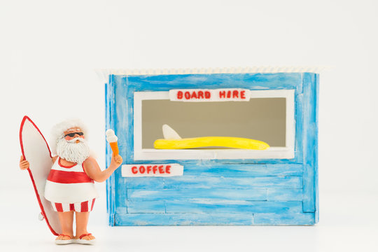 Concept image for making a lifestyle change showing Santa holding a surfboard and an ice cream while on vacation. There is a store in the background which sells coffee and also hires surfboards. 