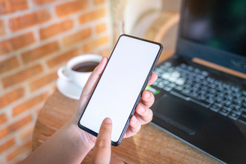 Woman holding smartphone with blank white screen on wooden table at coffee shop.Blank screen mobile phone with coffee cup.