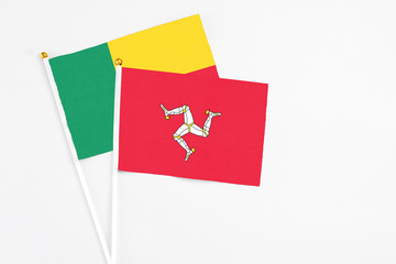 Isle Of Man and Benin stick flags on white background. High quality fabric, miniature national flag. Peaceful global concept.White floor for copy space.