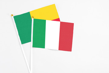 Italy and Benin stick flags on white background. High quality fabric, miniature national flag. Peaceful global concept.White floor for copy space.