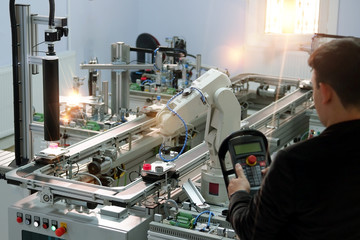 industry 4.0 concept: Man (engineer) is programming robotic arm with control panel (teach pendant) on smart factory production line background. Selective Focus.
