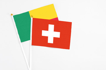 Obraz premium Switzerland and Benin stick flags on white background. High quality fabric, miniature national flag. Peaceful global concept.White floor for copy space.
