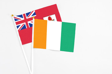 Cote D'Ivoire and Bermuda stick flags on white background. High quality fabric, miniature national flag. Peaceful global concept.White floor for copy space.