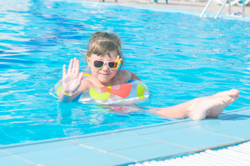 A child in a sunglasses is resting in the turquoise water of the pool. A little girl swims in the pool on an inflatable circle The concept of a fun children's holiday.