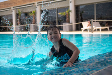 Caucasian toddler boy splashes his hand in a swimming pool