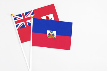 Obraz premium Haiti and Bermuda stick flags on white background. High quality fabric, miniature national flag. Peaceful global concept.White floor for copy space.