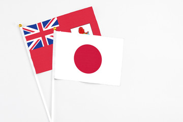 Japan and Bermuda stick flags on white background. High quality fabric, miniature national flag. Peaceful global concept.White floor for copy space.