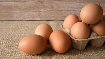 Brown chicken eggs in paper egg box on sackcloth and wooden background. Healthy food concept