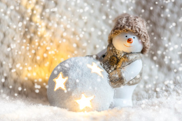 Obraz premium Toy snowman in a knitted hat, with a luminous ball close up on a white background, front view. New Year and Christmas background for greetings, banner, postcard, advertisement, Copy space, place for t