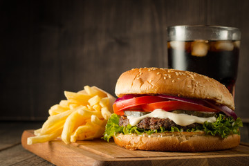 Home made hamburger with beef, onion, tomato, lettuce and cheese. Fresh burger close up on wooden rustic table with potato fries, beer and chips. Cheeseburger.