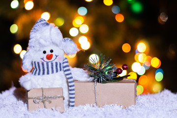 Snowman and boxes with gifts on a bokeh background. Copy space, front view. Holiday, New Year's Eve, Christmas background for congratulations, banner, postcards, advertising with a place for text.