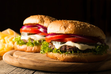 Home made hamburger with beef, onion, tomato, lettuce and cheese. Fresh burger close up on wooden rustic table with potato fries, beer and chips. Cheeseburger.