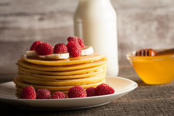 Tasty pancakes with blackberries, banana, raspberries, eggs, honey and maple syrup on wooden background. Morning breakfast concept.