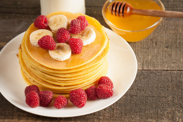 Tasty pancakes with blackberries, banana, raspberries, eggs, honey and maple syrup on wooden background. Morning breakfast concept.