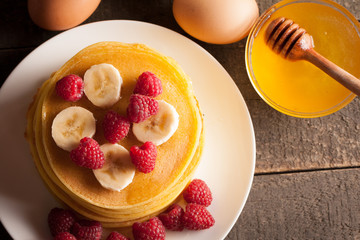Tasty pancakes with blackberries, banana, raspberries, eggs, honey and maple syrup on wooden background. Morning breakfast concept.