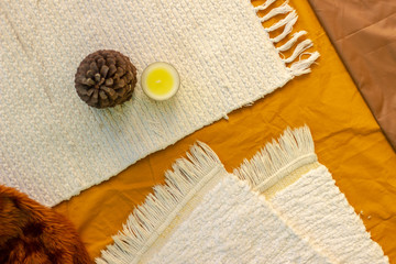 Tree cone and yellow scented candle on fabric carpet background flatlay, top view 