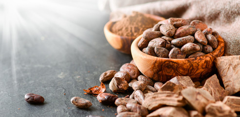 Cocoa raw beans in bowl and dark chocolate on black stone table.