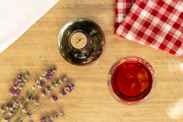 Red wine glass and bottle with lavender and checked cloth on wooden table, romantic flatlay, top view 