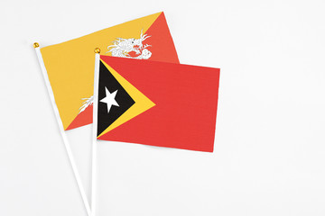 Obraz premium East Timor and Bhutan stick flags on white background. High quality fabric, miniature national flag. Peaceful global concept.White floor for copy space.