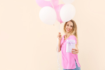 Beautiful young woman with balloons and gift on color background