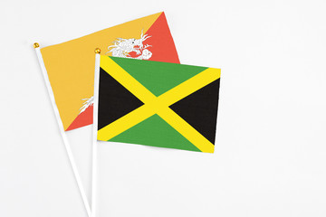 Jamaica and Bhutan stick flags on white background. High quality fabric, miniature national flag. Peaceful global concept.White floor for copy space.